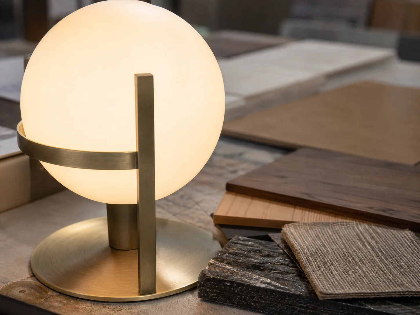 Détail de luminaire design en verre opalin et métal près d’échantillons de matières